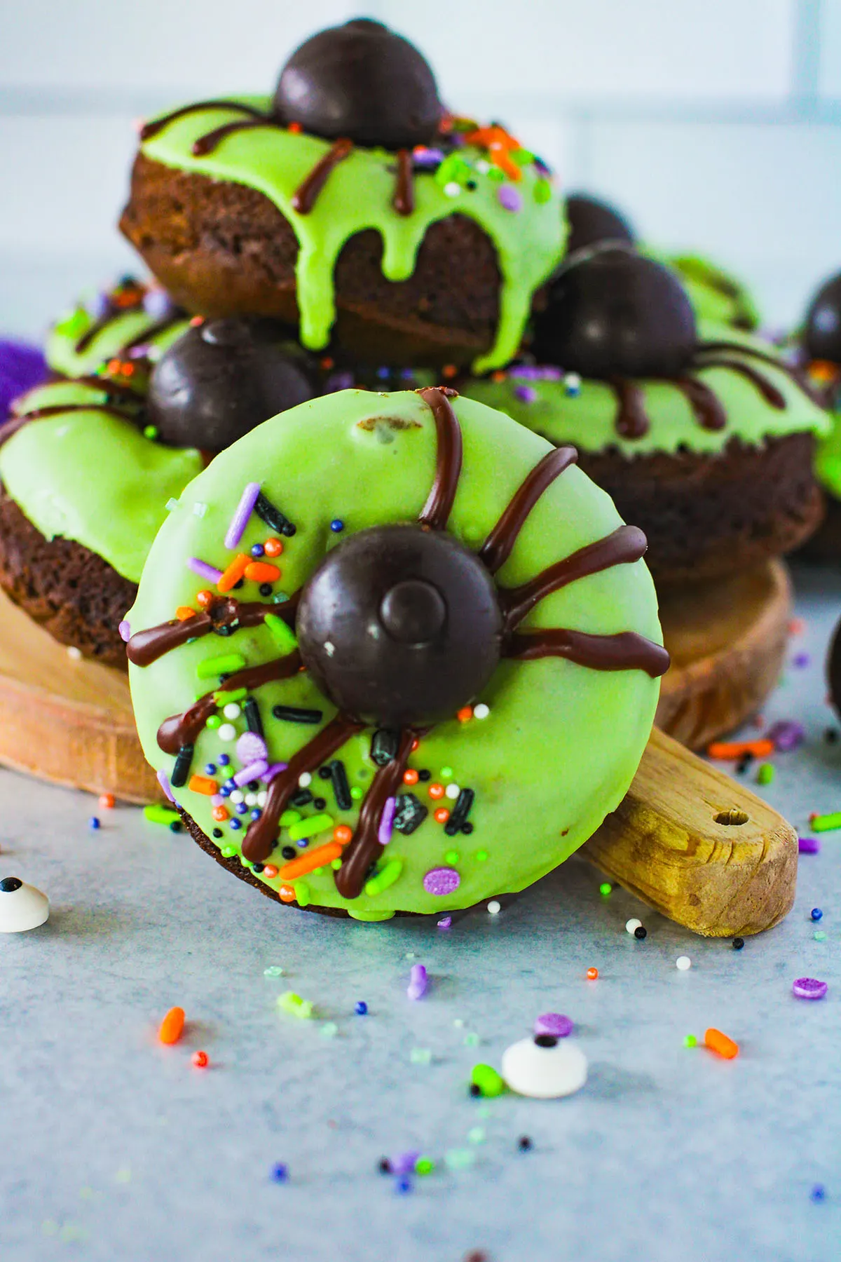 Spider Donuts with green icing on a wooden serving board.