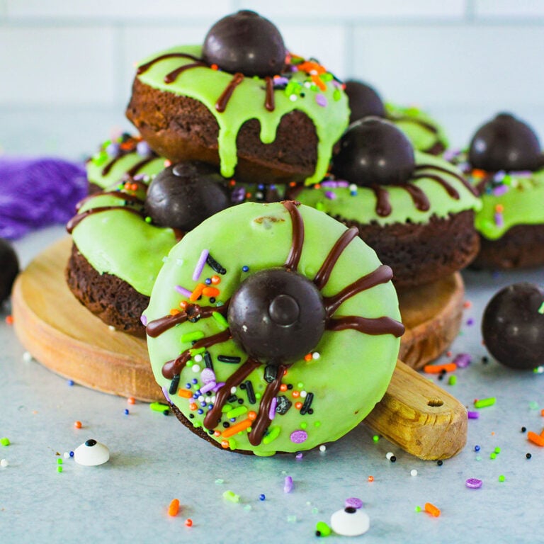 Spider Donuts with green icing on a round serving board.