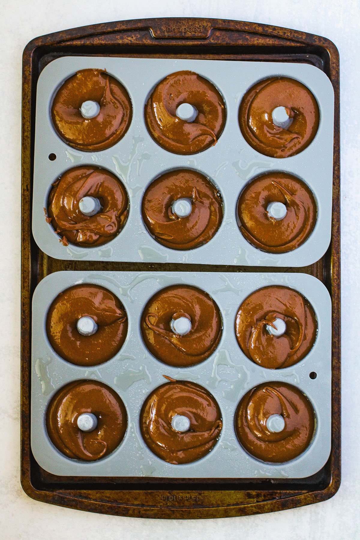 Chocolate donut batter is poured into a donut pan.