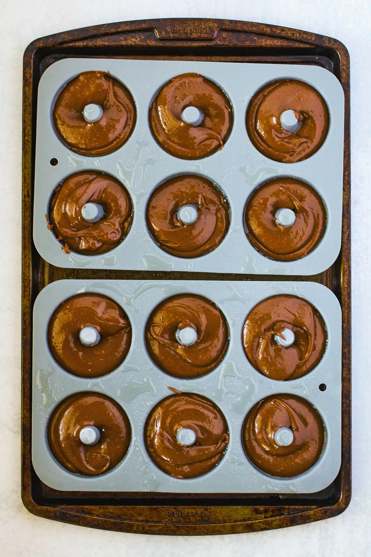 Chocolate donut batter is poured into a donut pan.