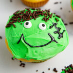 Decorated Frankenstein cupcake with chocolate sprinkles on the counter.