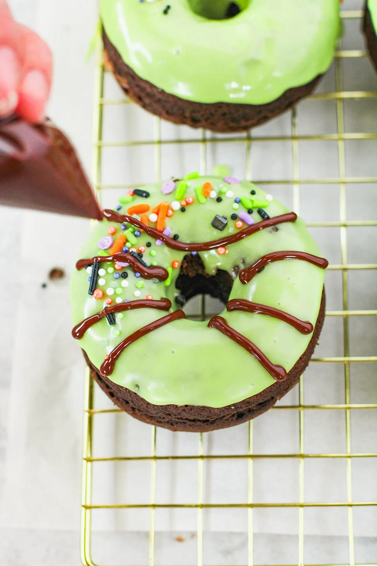 Piping chocolate glazed spider legs to a green glazed chocolate donut.