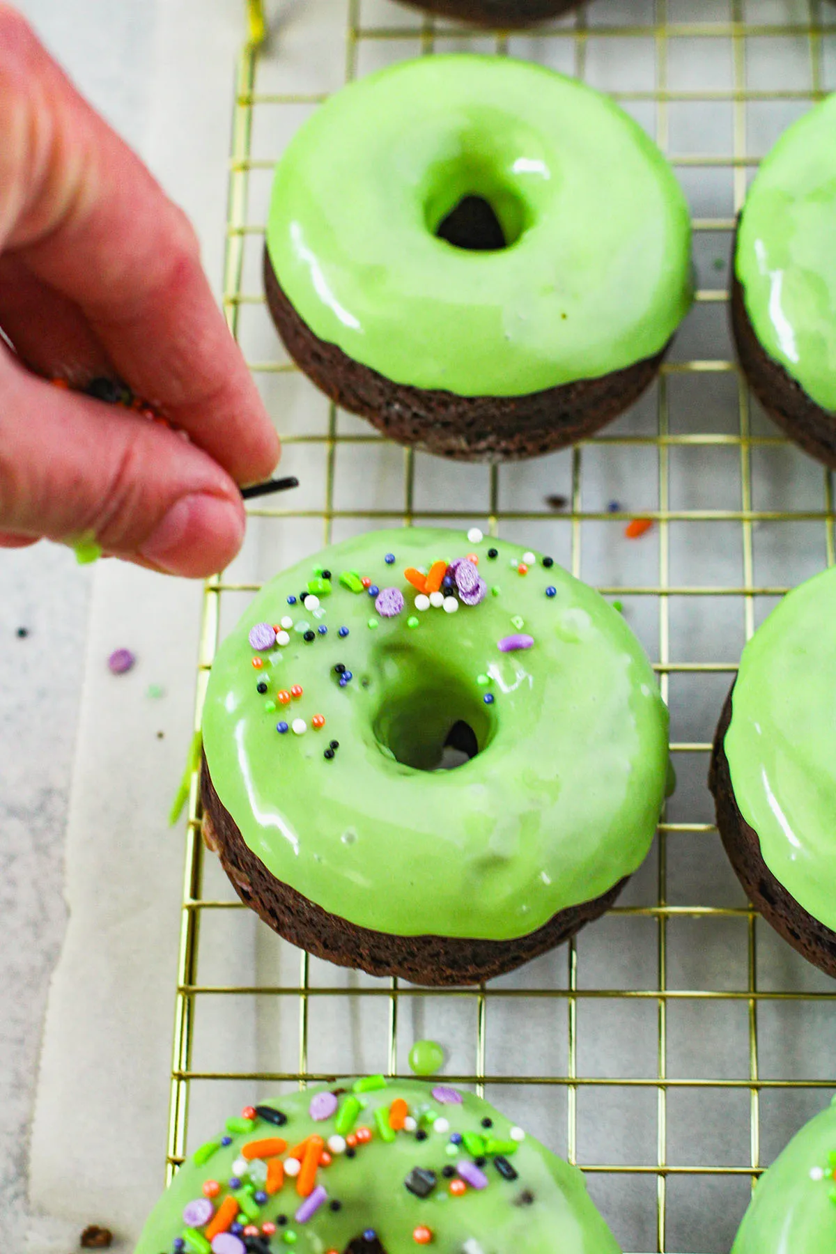 Topping green glazed donuts with Halloween sprinkles.