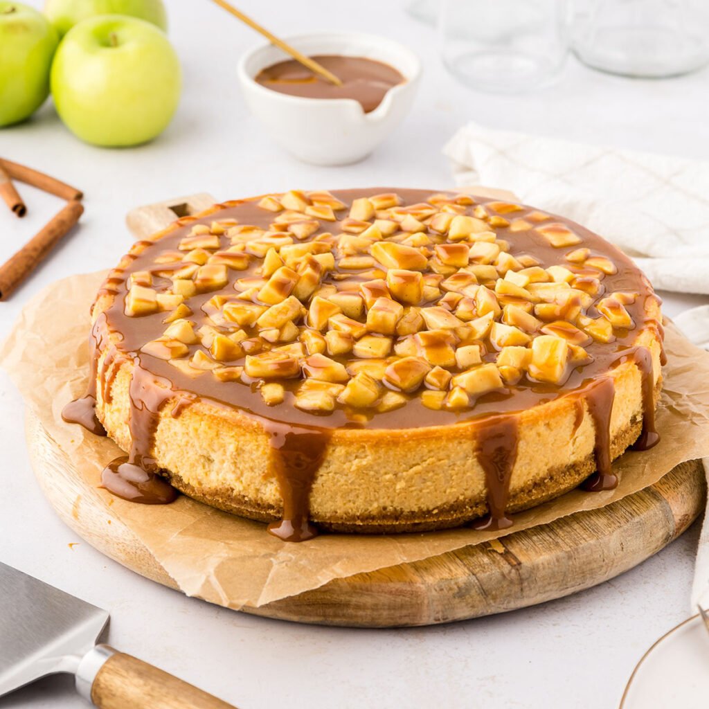 Caramel Apple Cheesecake is on a parchment paper-lined round wooden serving board.