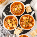 Three white bowls of pot roast soup served on a black round platter with crackers.