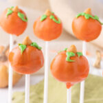 Five Pumpkin Cake Pops topped with butterscotch chip and green icing stems.