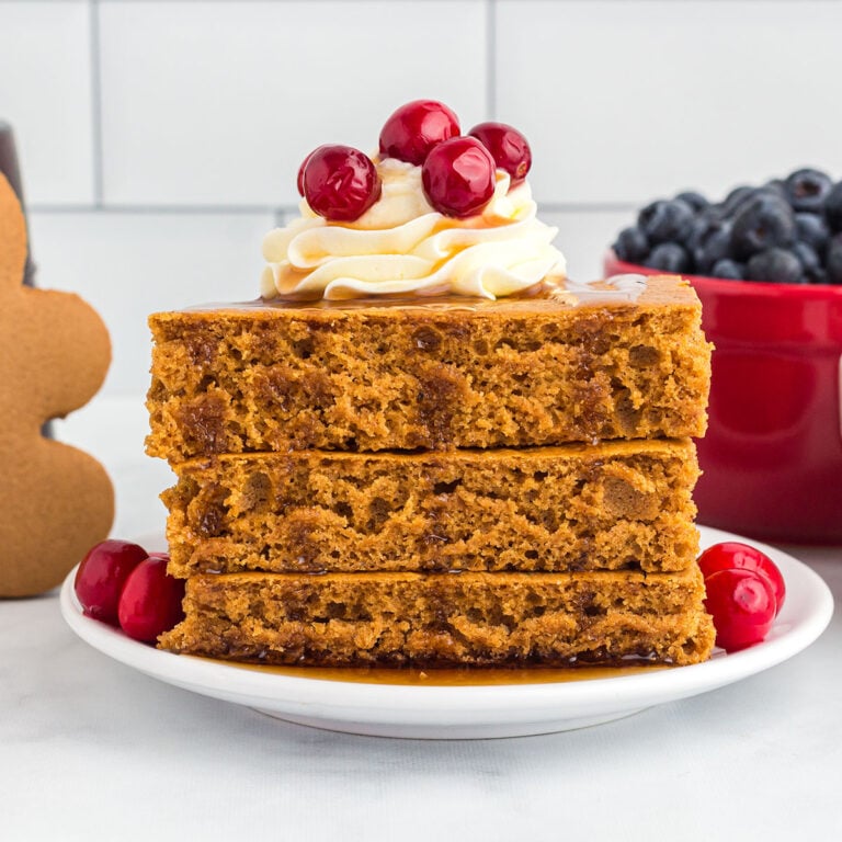Gingerbread Pancakes on a white plate served with whipped cream on top.