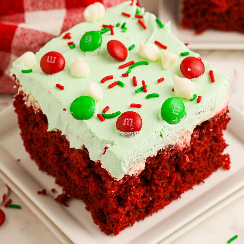 A slice of Red Velvet Christmas Poke Cake on a white square plate.