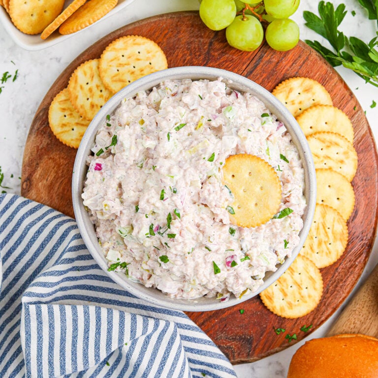 Ham Salad in a bowl served on round wooden board with crackers and grapes.