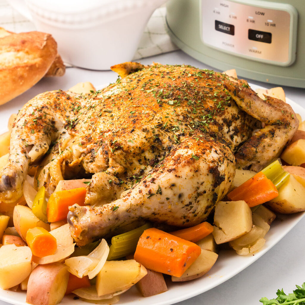 Whole Chicken served on a white platter with carrots and potatoes.