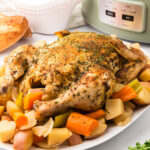 Whole Chicken served on a white platter with carrots and potatoes.