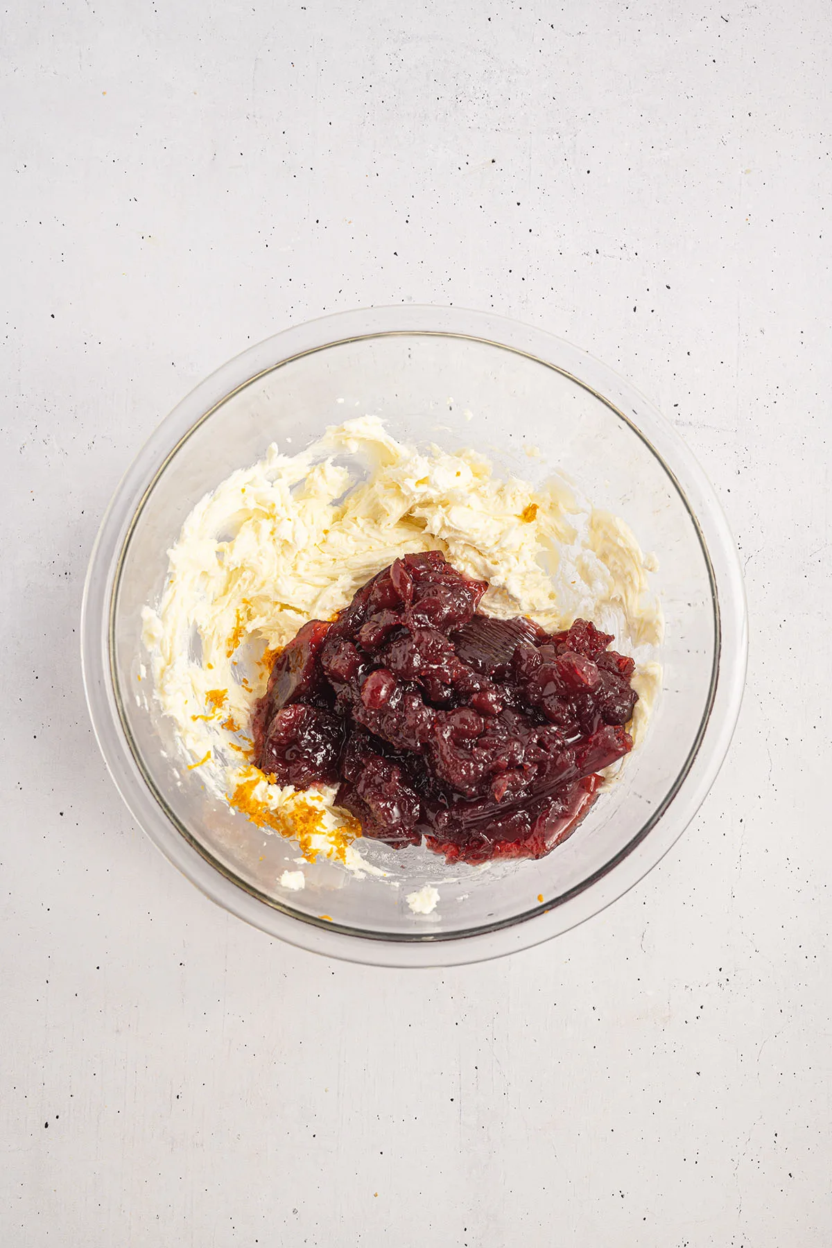 Cream cheese, sugar, orange zest, and cranberry sauce in a glass mixing bowl.