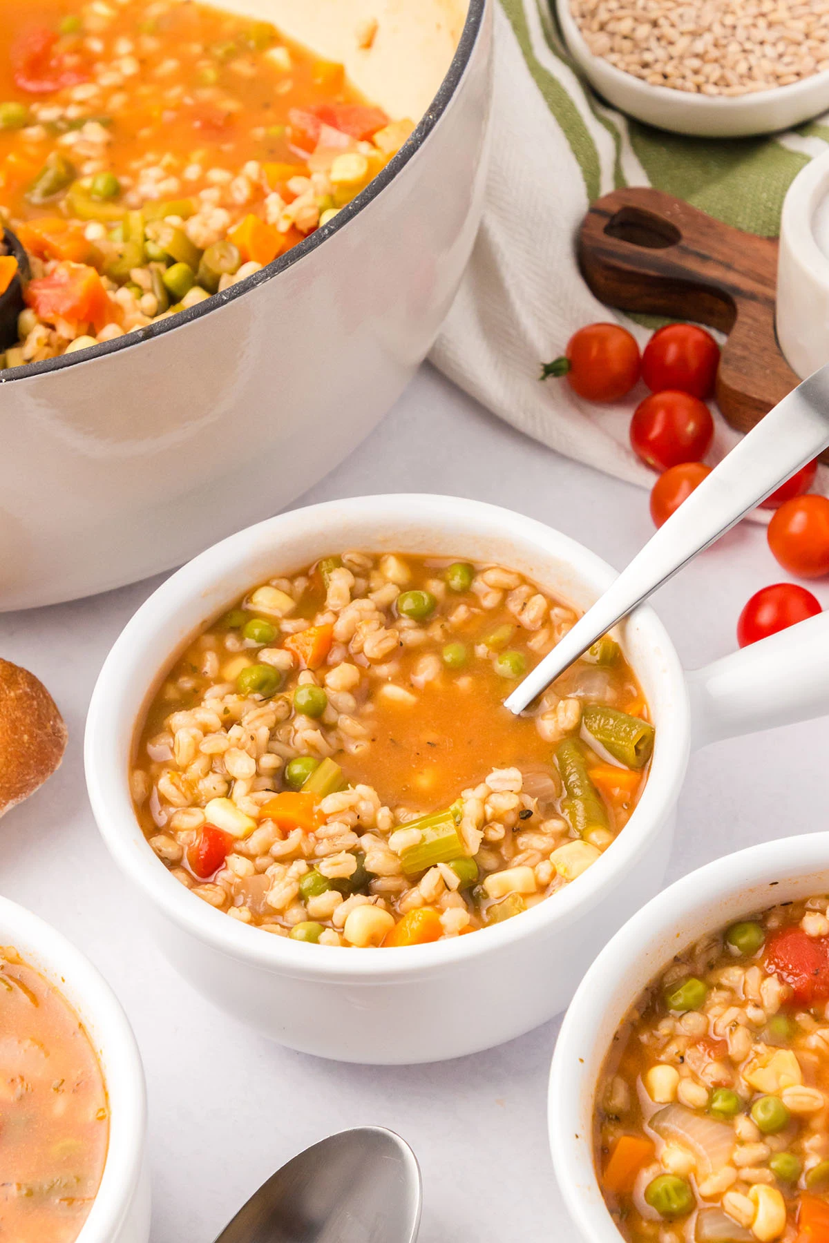 Vegetable barely soup in a white bowl with a spoon.