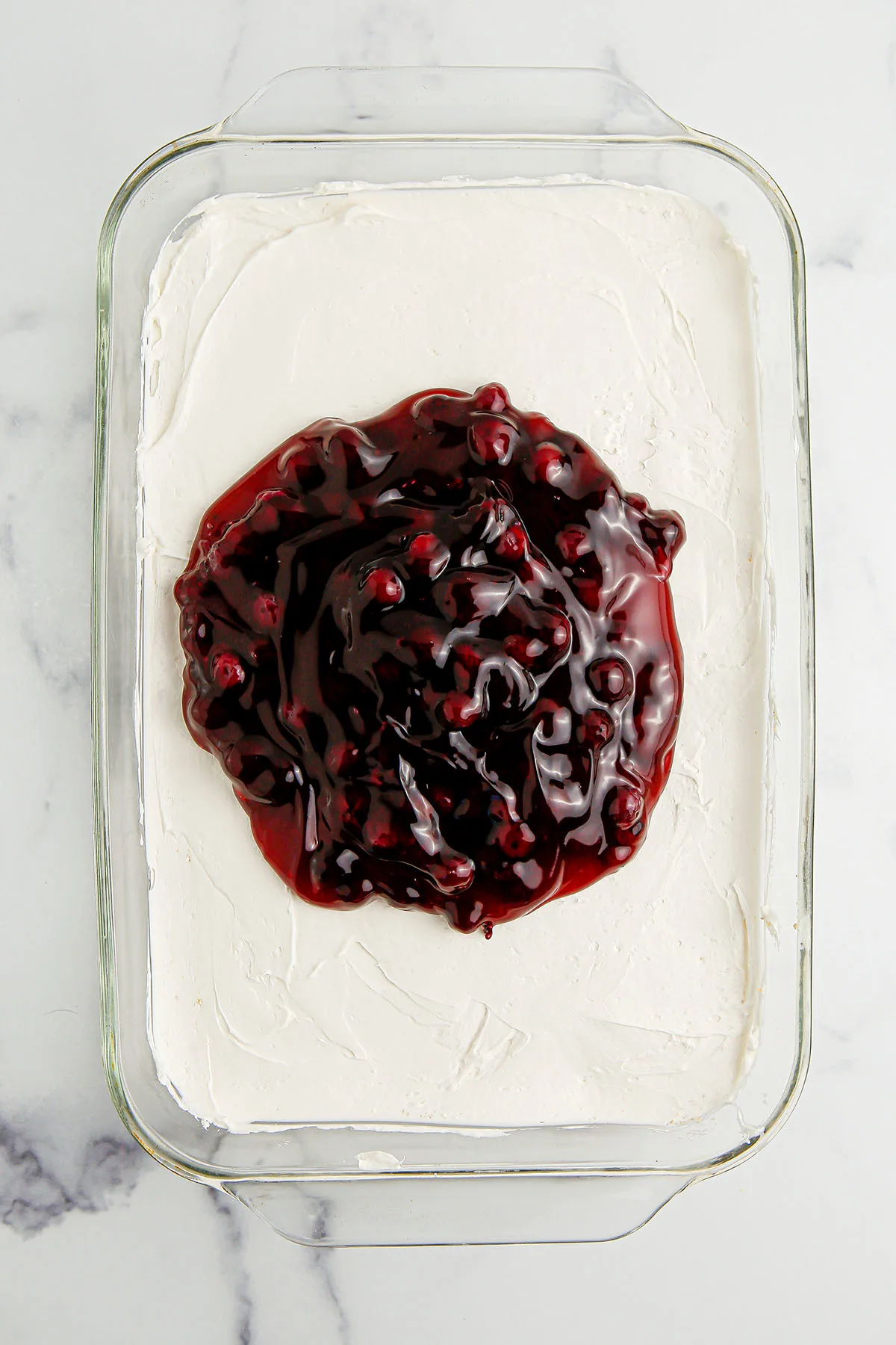 Blueberry pie filling poured over the cheesecake layer in glass dish.