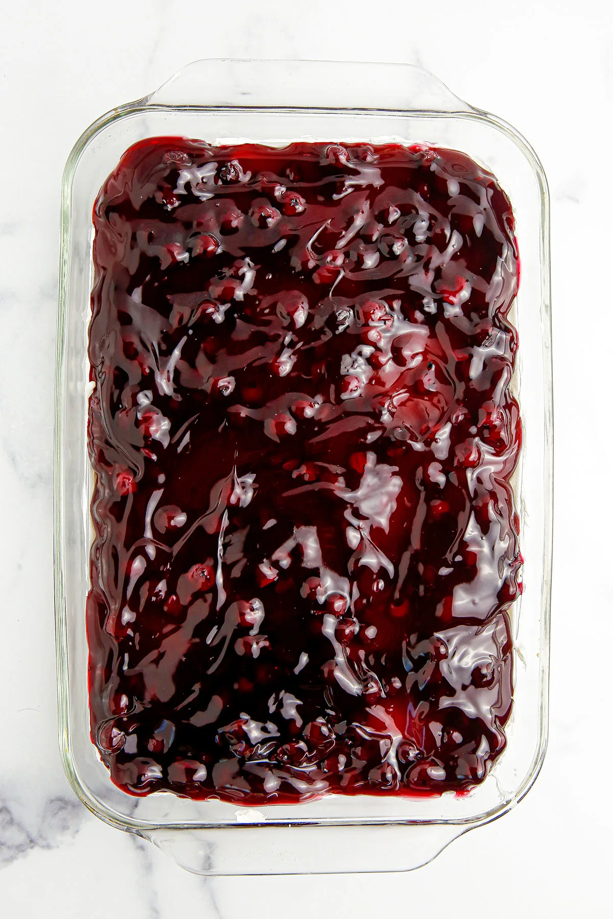 Blueberry pie filling spread over the cheesecake layer in glass dish.
