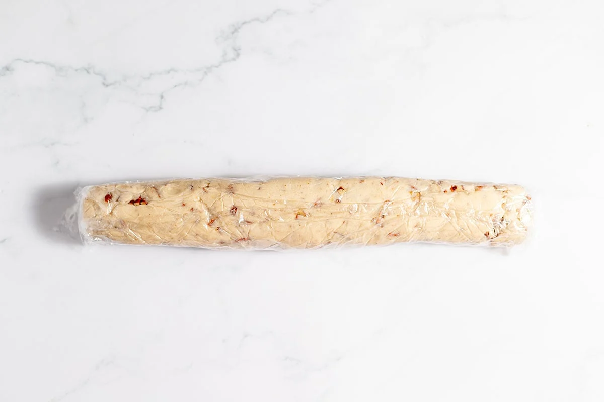 Pecan Shortbread Cookie dough shaped into a log and rolled up in plastic wrap.
