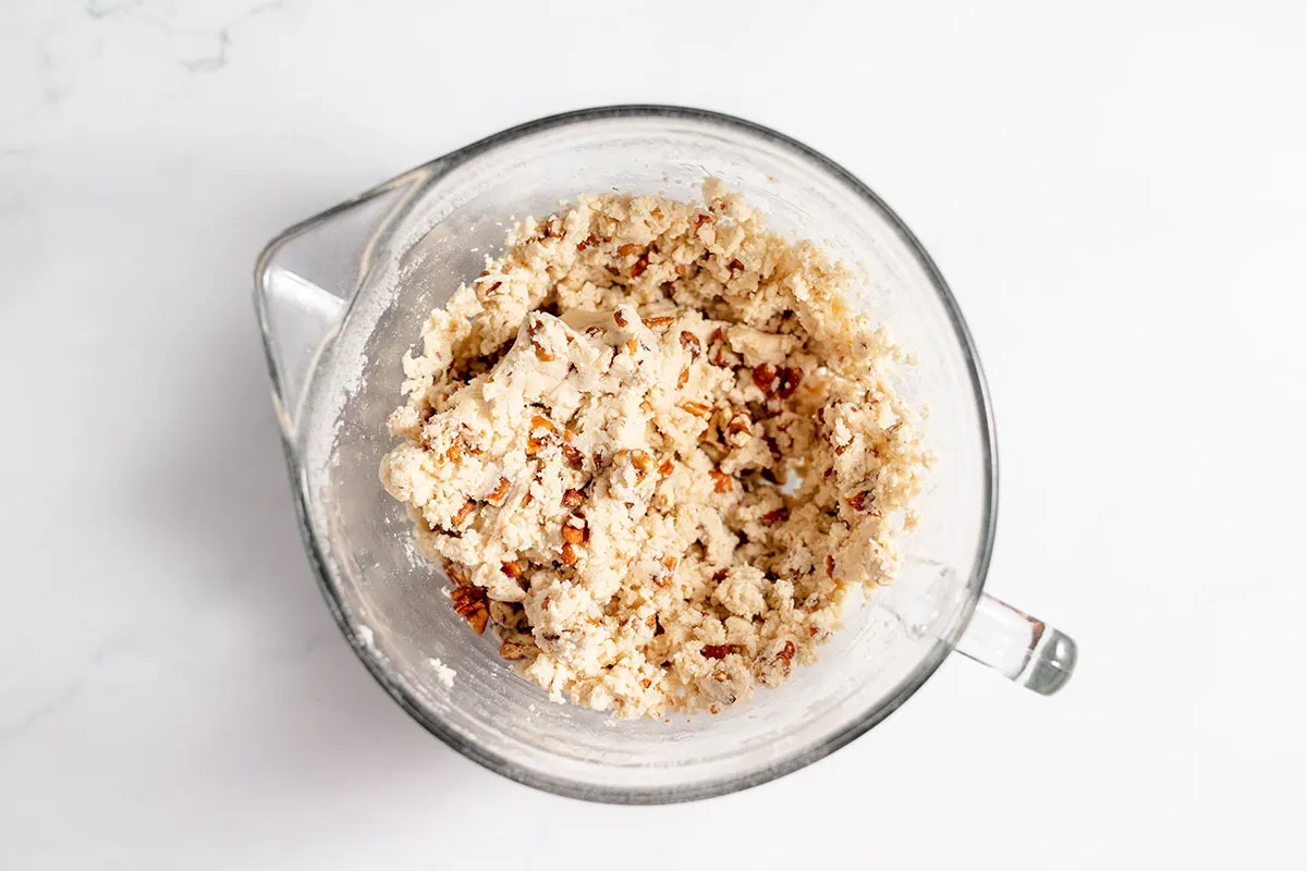 Pecans mixed into the cookie dough in the glass mixing bowl.