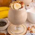 Banana Breakfast Smoothie served in a stemmed glass topped with sliced bananas and nuts.