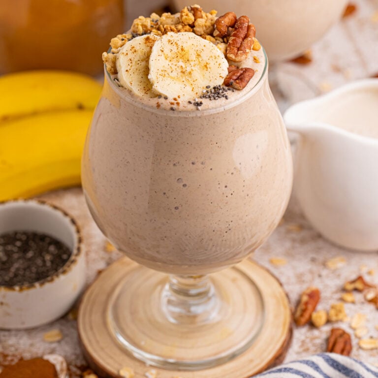 Banana Breakfast Smoothie served in a stemmed glass topped with sliced bananas and nuts.