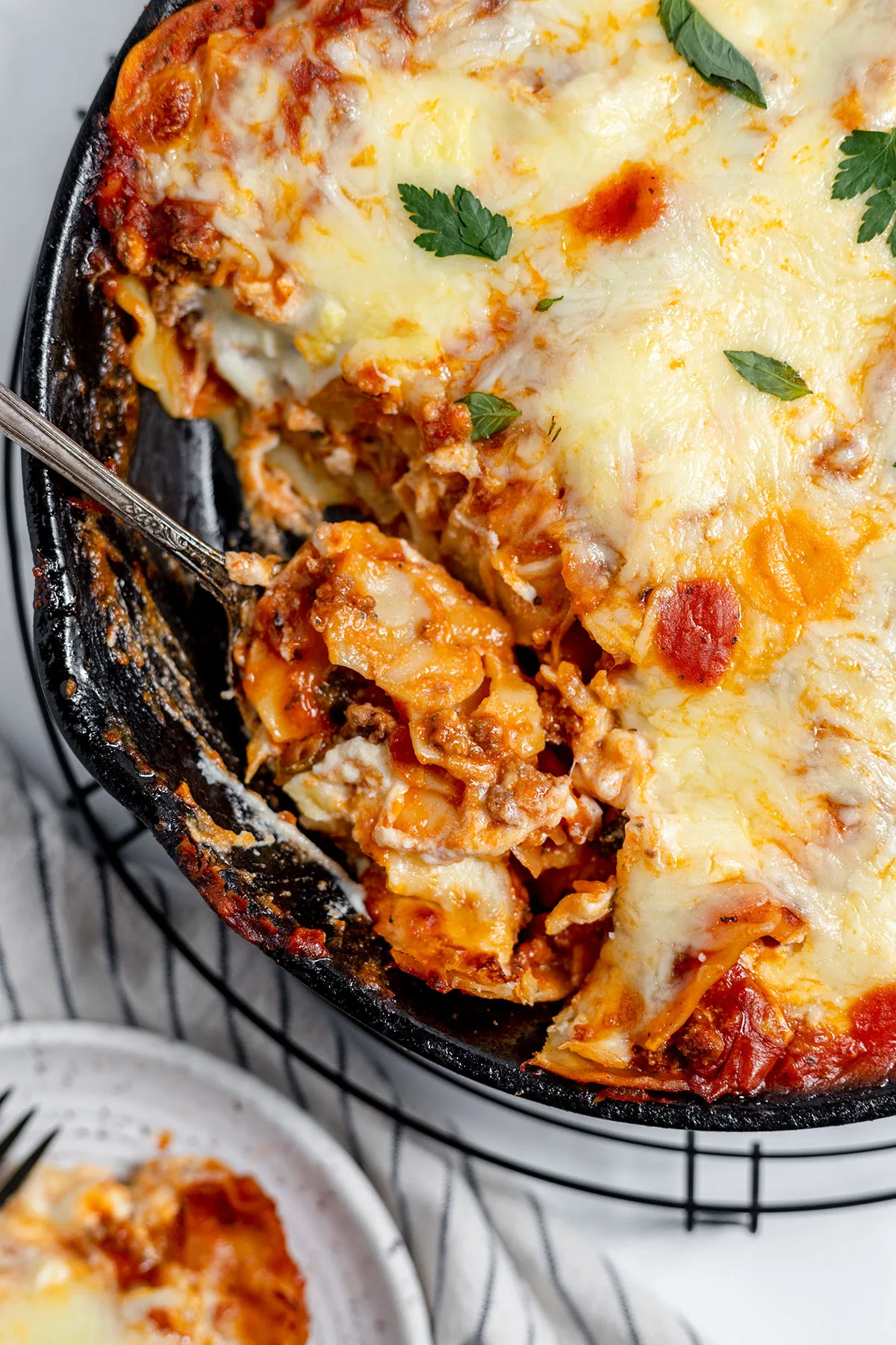 Lasagna in a cast iron skillet with a serving on a spoon.