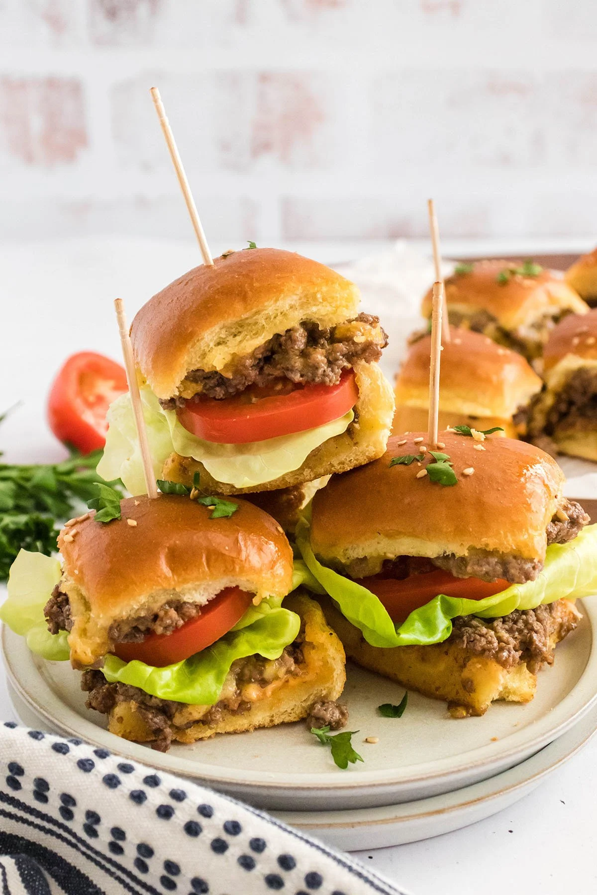 Cheeseburger Sliders on Hawaiian Rolls with lettuce and tomatoes on a white plate.