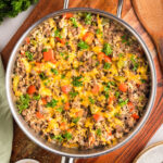 Hamburger Rice Skillet topped with shredded cheddar cheese served on a wooden board.
