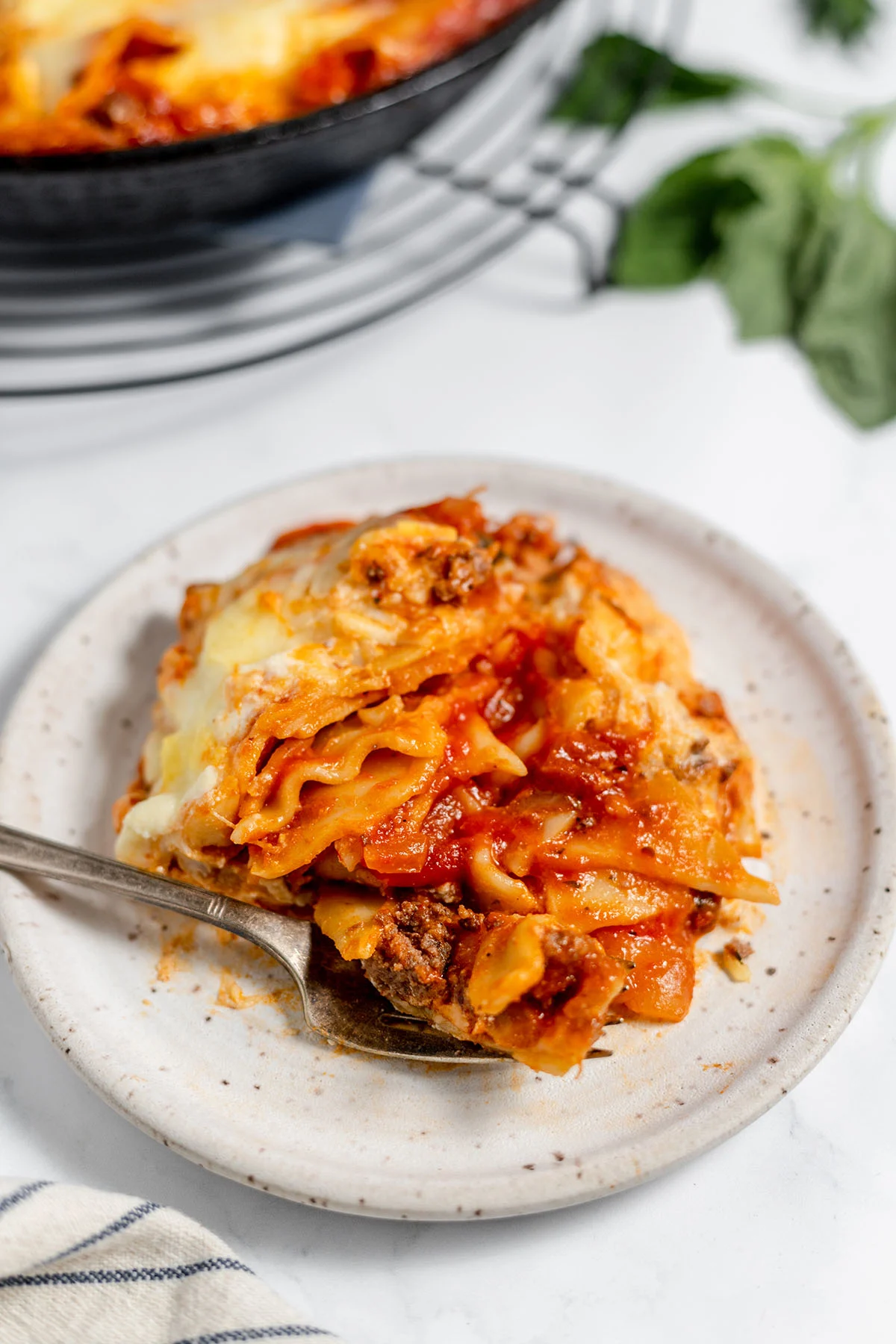 A serving of Lasagna on a white plate with a fork.