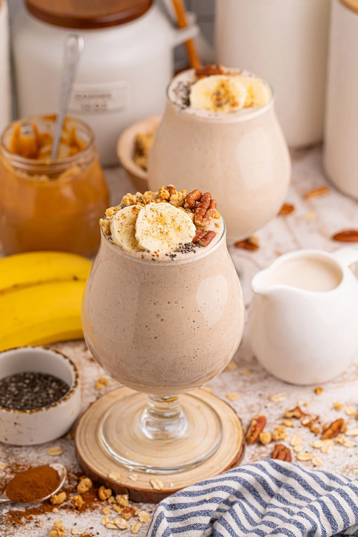 Two Banana Breakfast Smoothies served in stemmed glasses and topped with sliced bananas and nuts.
