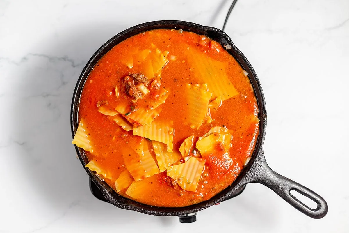 Broken lasagna noodles are added to the ground beef mixture in the cast iron skillet.