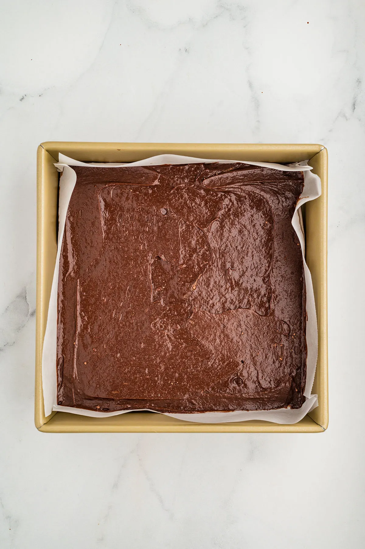 Brownie batter is in a parchment paper-lined baking pan.