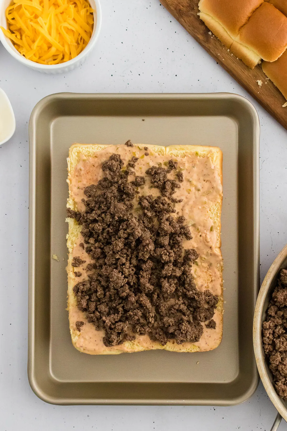 Cooked ground beef spread on top of the cheeseburger sauce on the bottom half of the Hawaiian rolls.