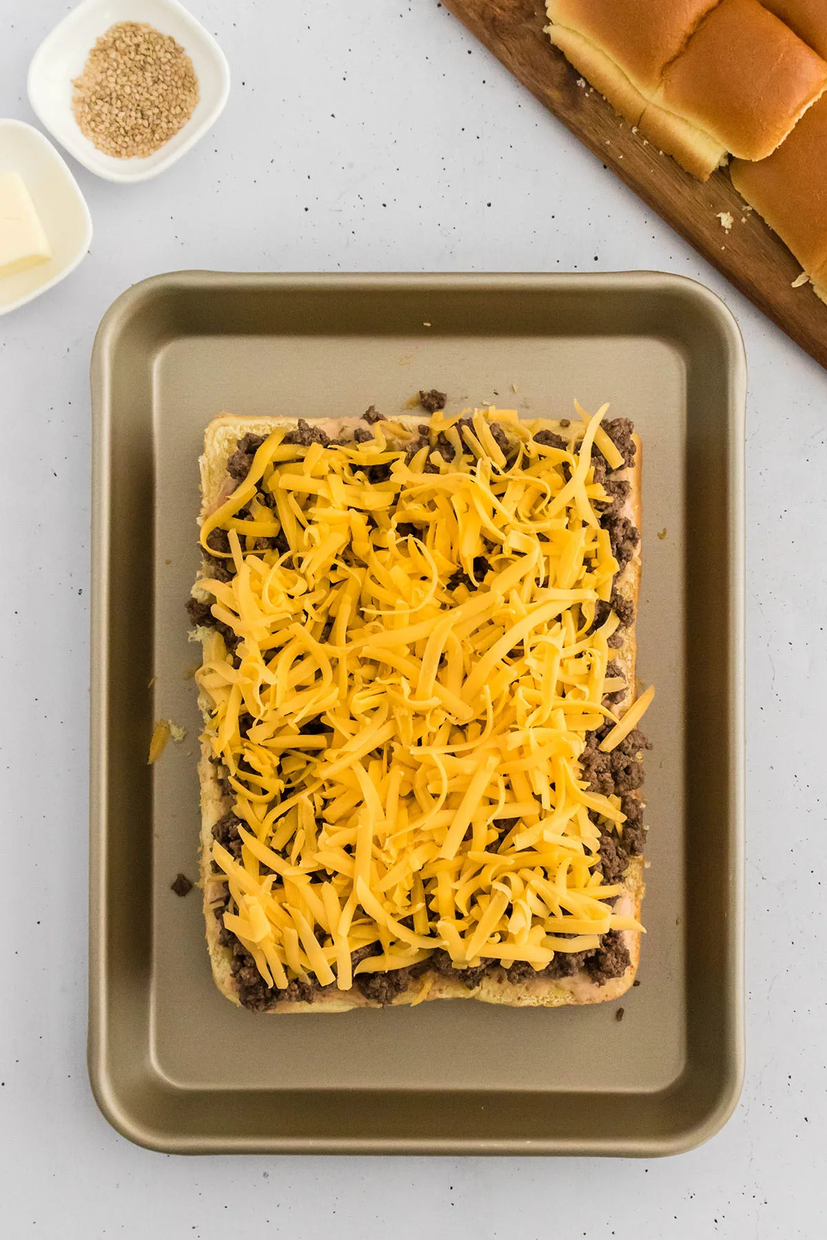 A layer of cheddar cheese spread over the cooked ground beef on Hawaiian rolls.