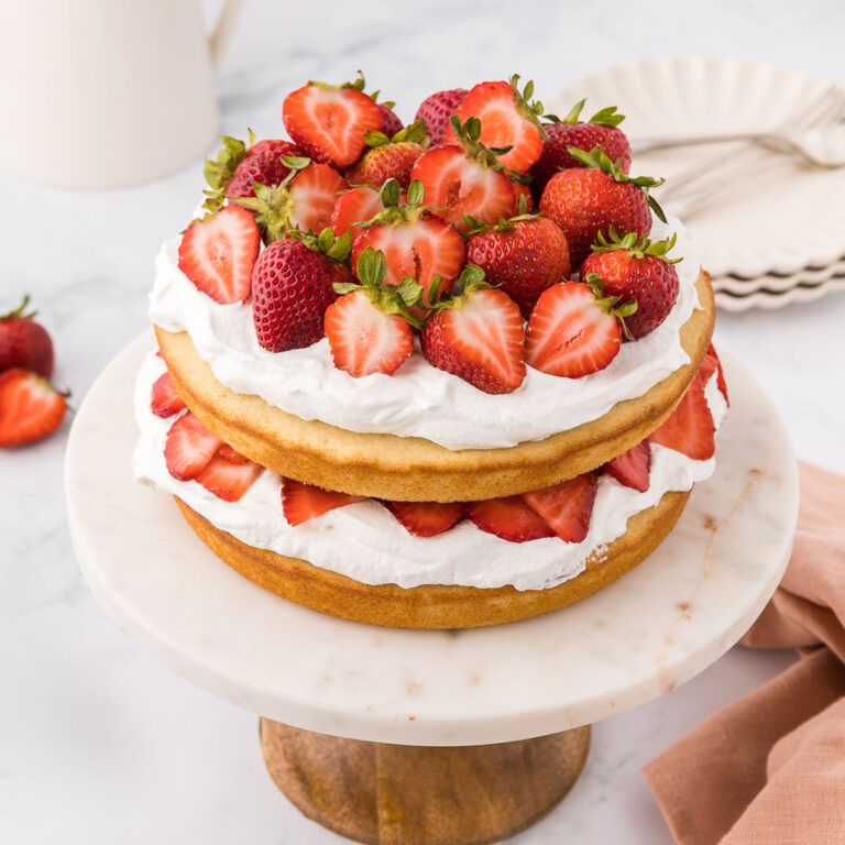 Strawberry Layer Cake on a cake stand topped with fresh strawberries.