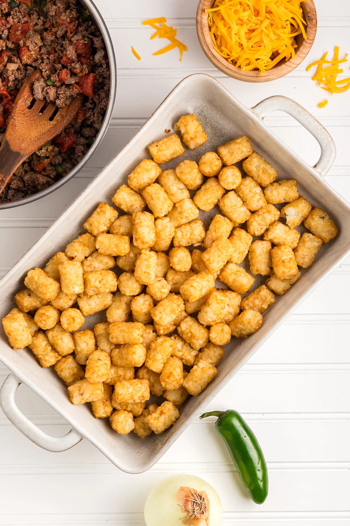 Cooked tater tots in the bottom of a baking dish.