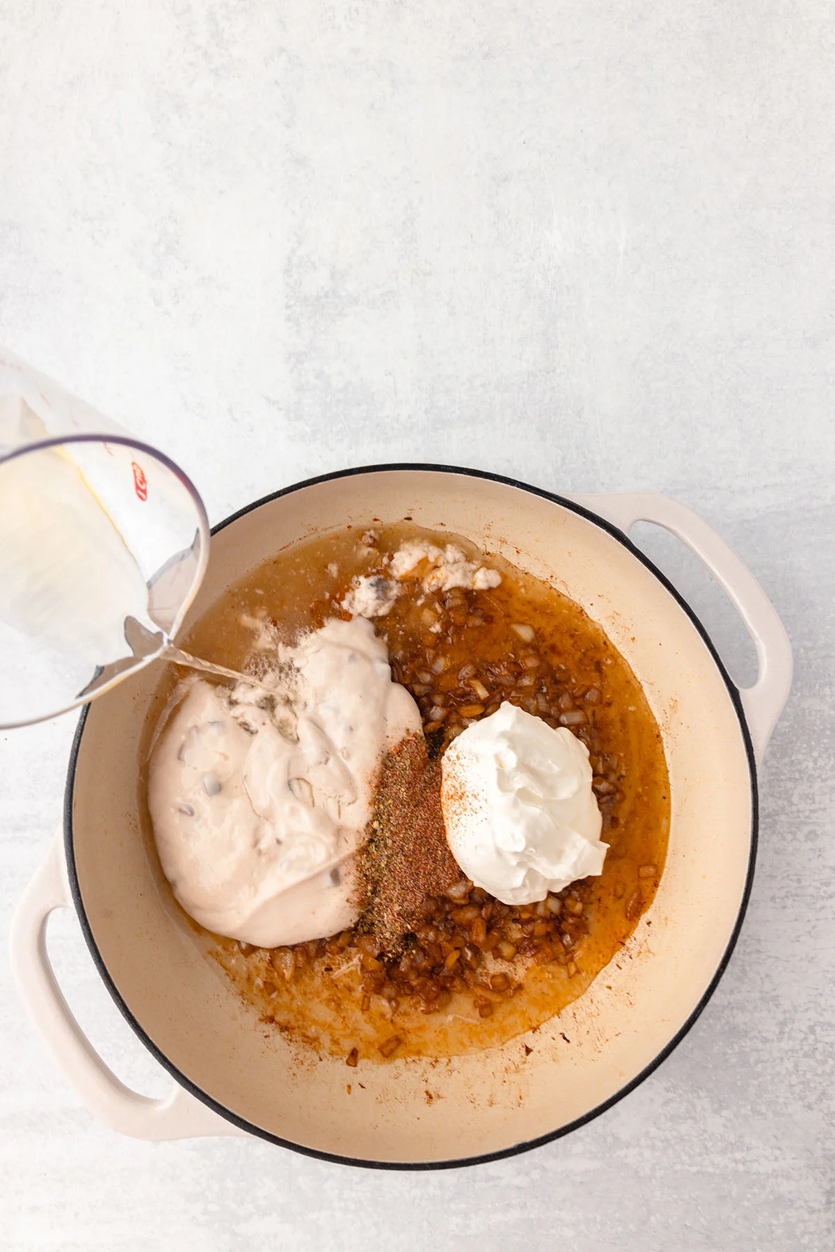 Cream of mushroom soup, sour cream, and chicken broth are added to the onions in the skillet.