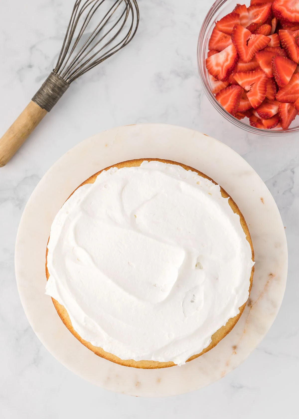 Whipped cream is spread over the top of the round cake.