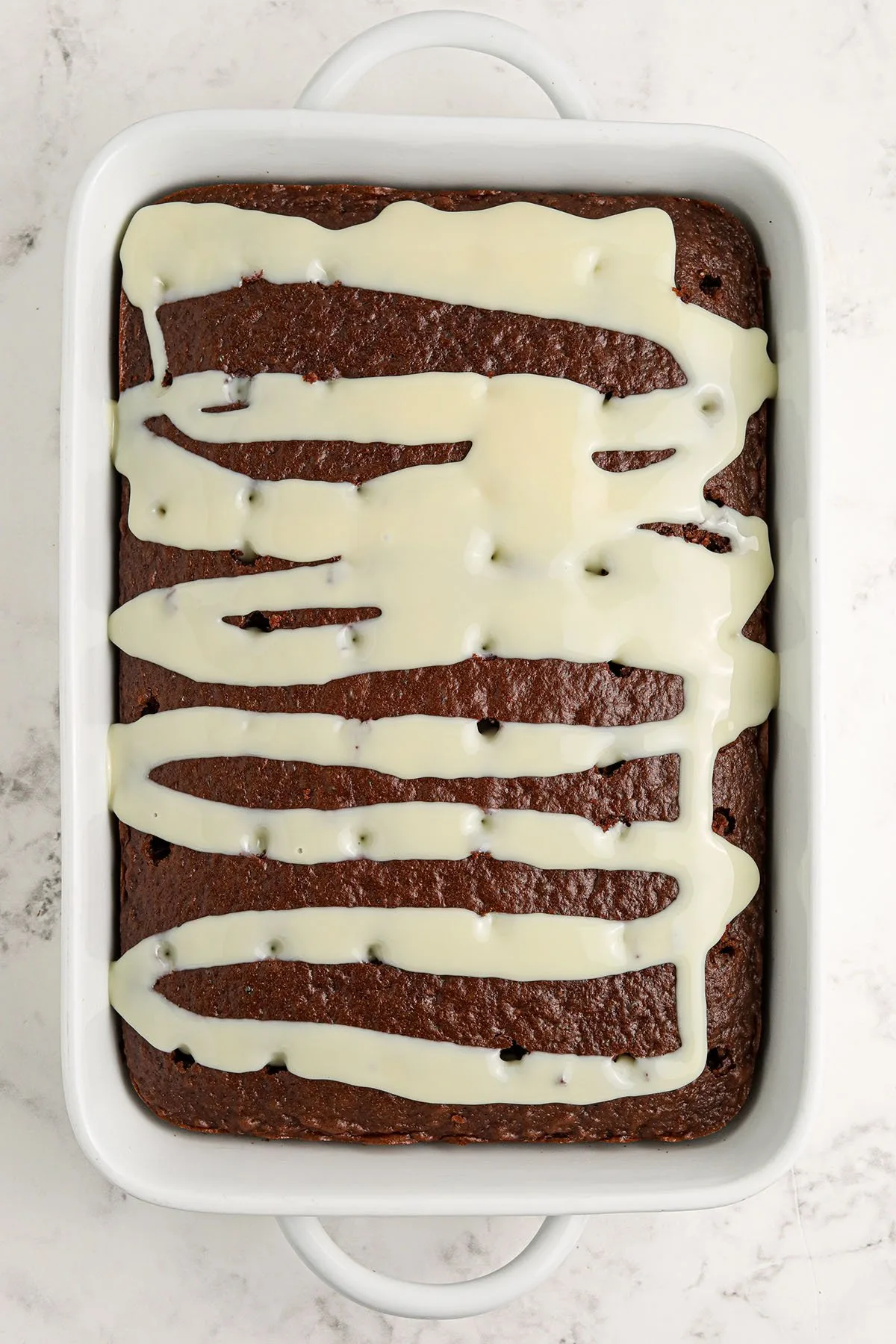 Sweetened condensed milk poured over the baked chocolate cake in the baking dish.