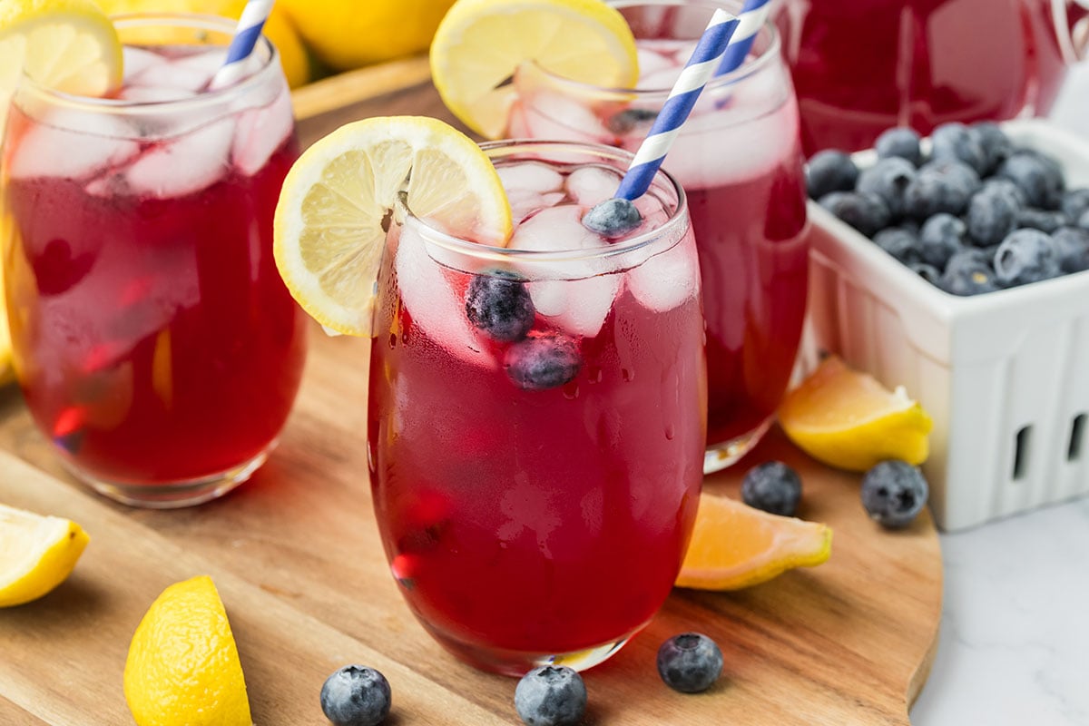 Blueberry Lemonade served in a glass with a straw and a slice of lemon.