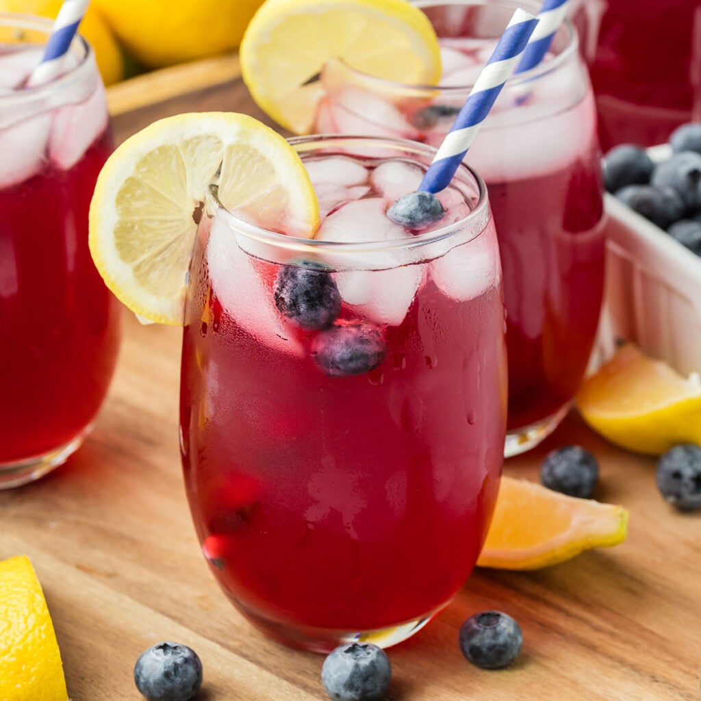 A glass of Blueberry Lemonade with a straw and a slice of lemon.