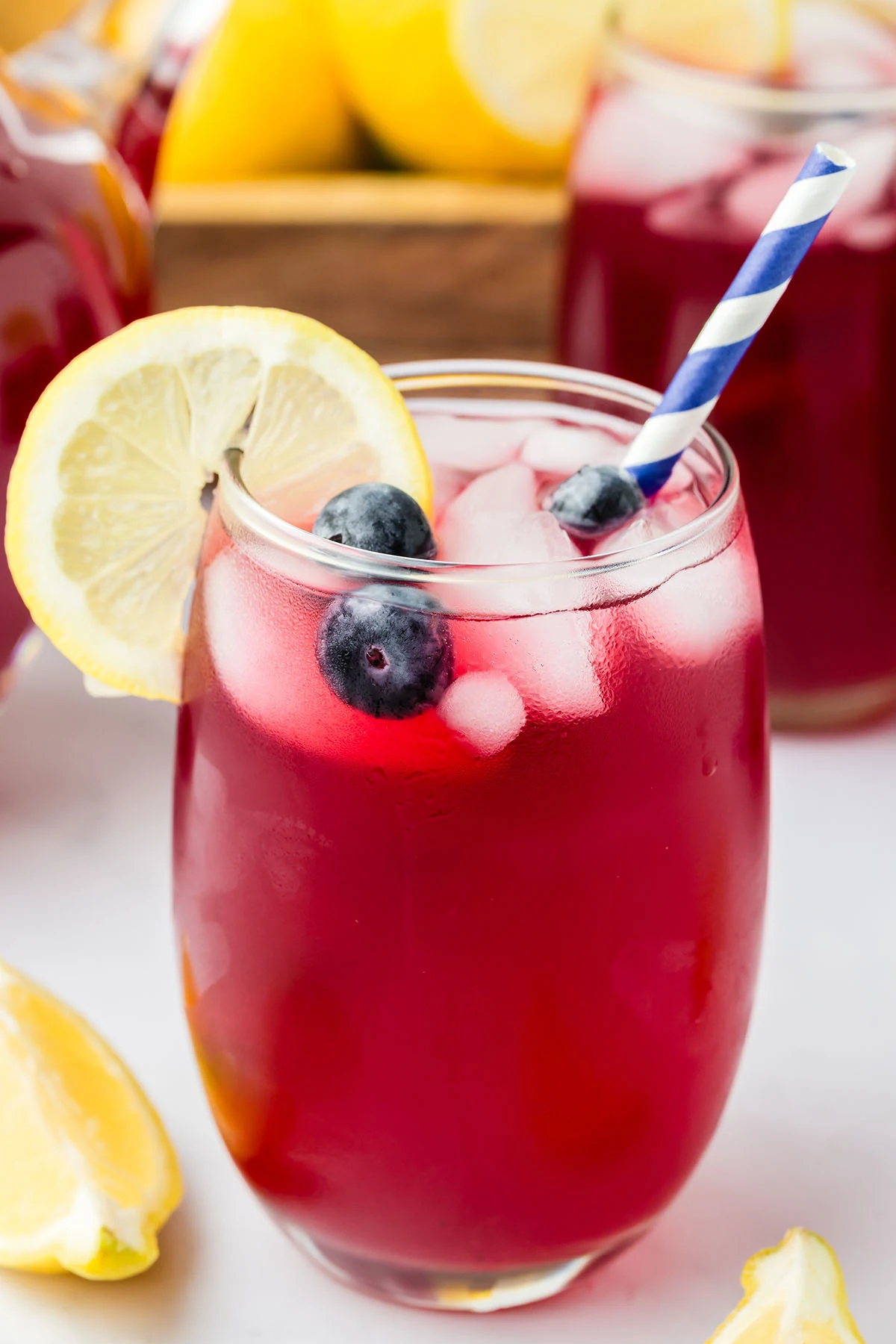 Blueberry Lemonade in a glass with a straw and a slice of lemon.