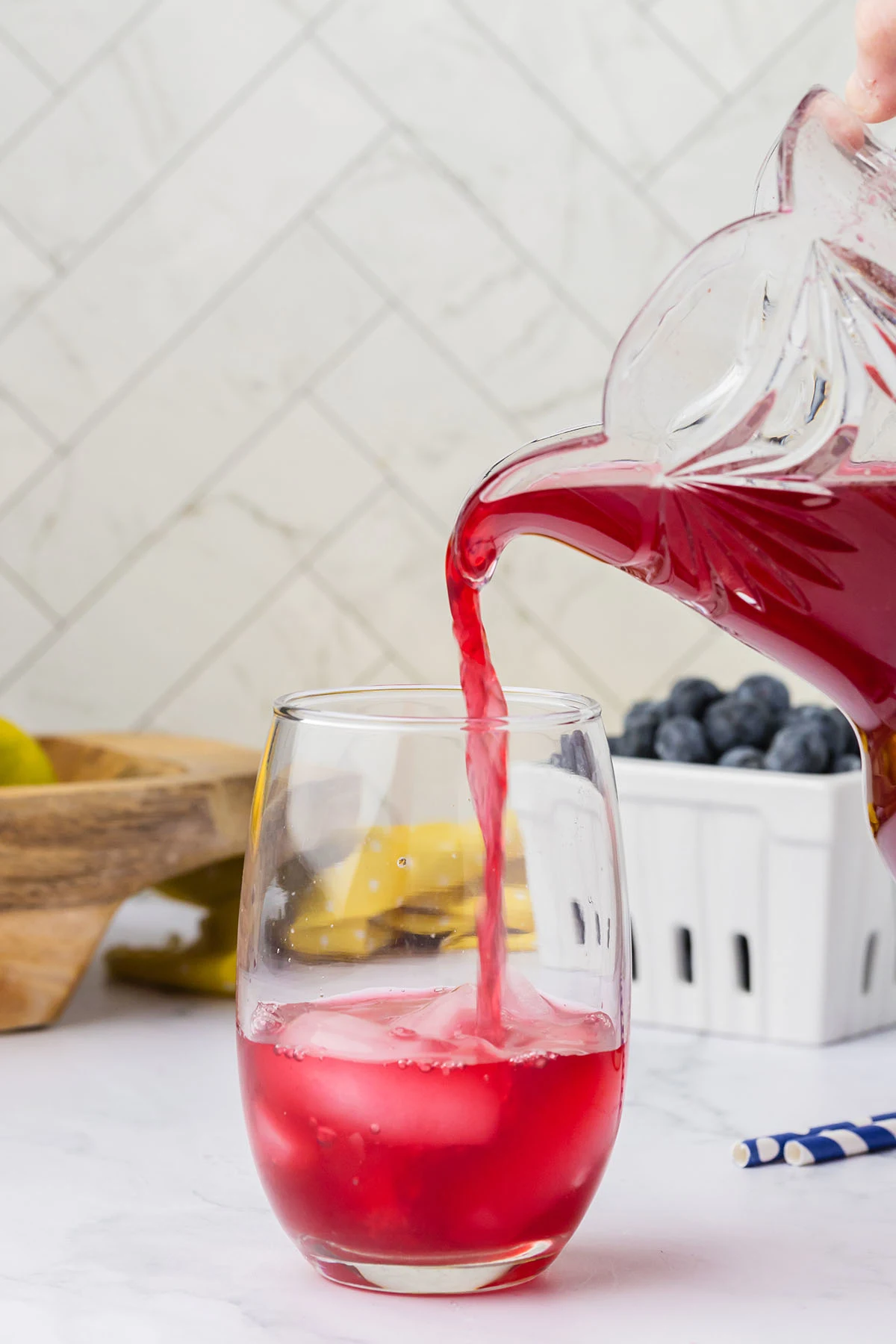 Blueberry Lemonade is being poured into a glass with ice.