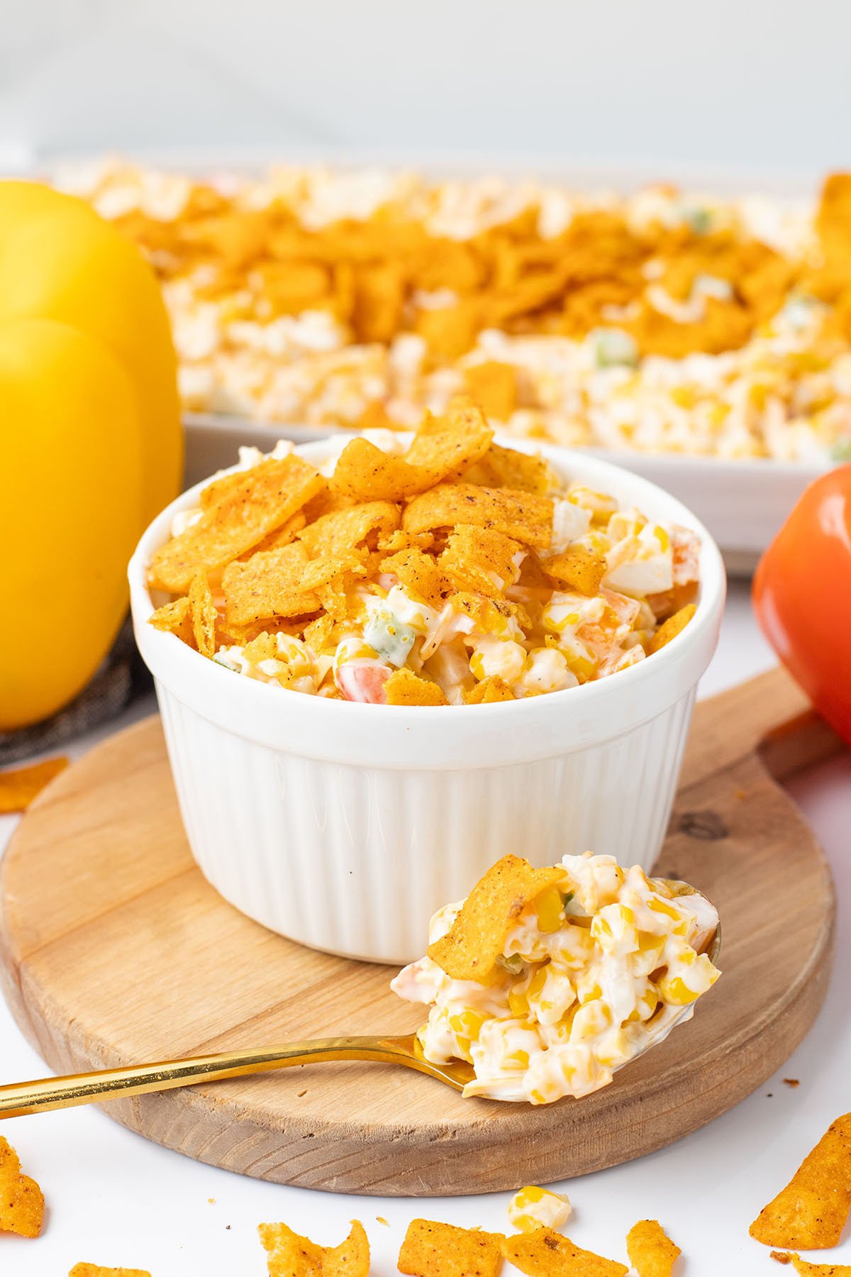 Frito Corn Salad served in a white bowl on a wooden board with a scoop on a spoon.