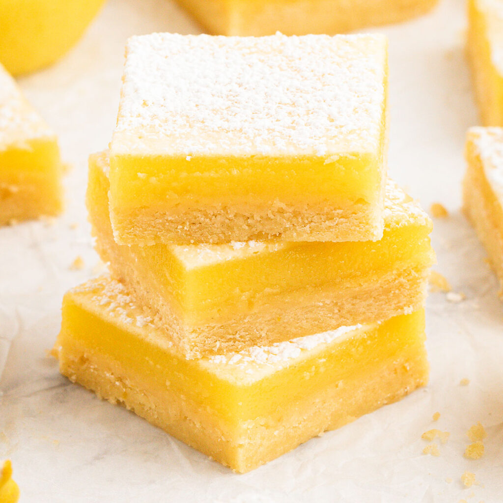 Three Lemon Bars stacked on parchment paper.