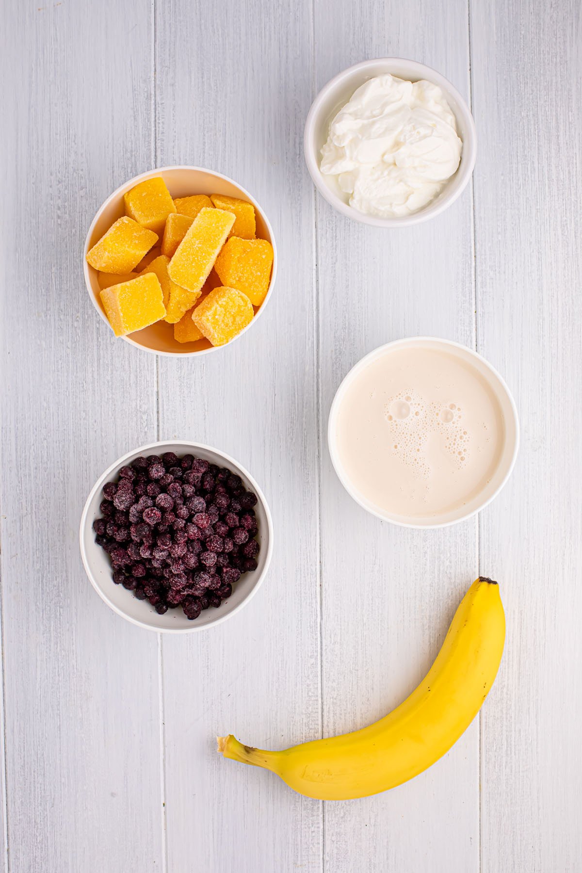 Ingredients for a blueberry mango smoothie are set out on the counter.
