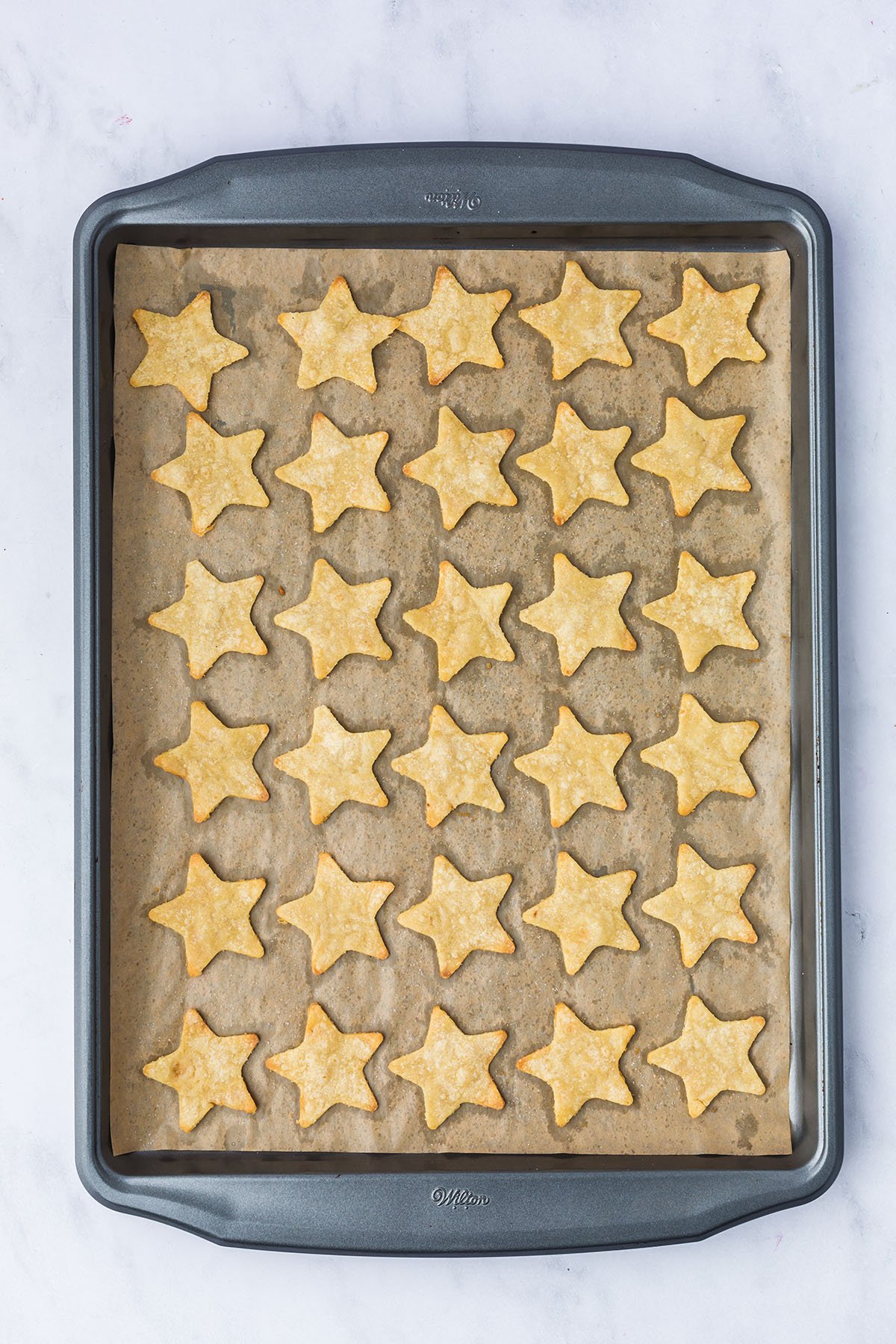 Baked star tortilla chips on a parchment paper lined baking sheet.