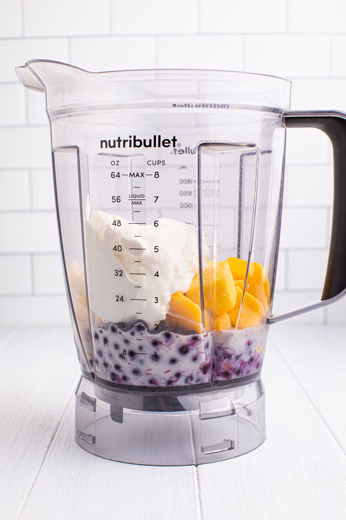 Frozen blueberries, frozen mango chunks, a sliced banana, yogurt, and milk in a blender.