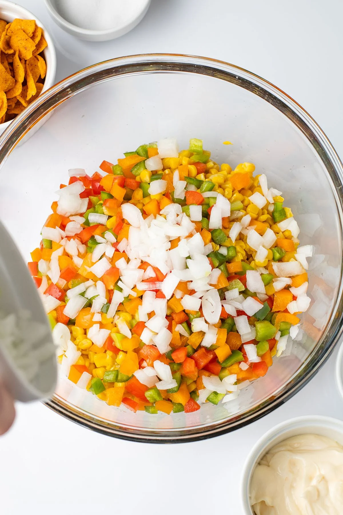 Corn, diced onion, and bell peppers in a glass mixing bowl.