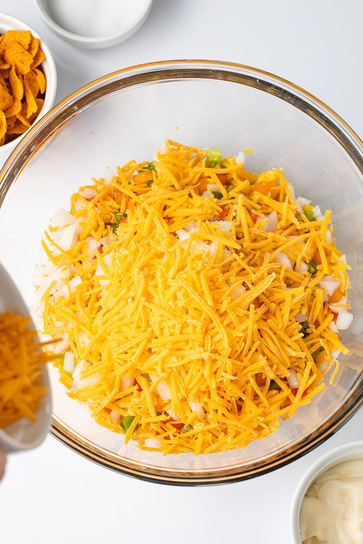 Corn, diced onion, bell peppers, and cheese in a glass mixing bowl.