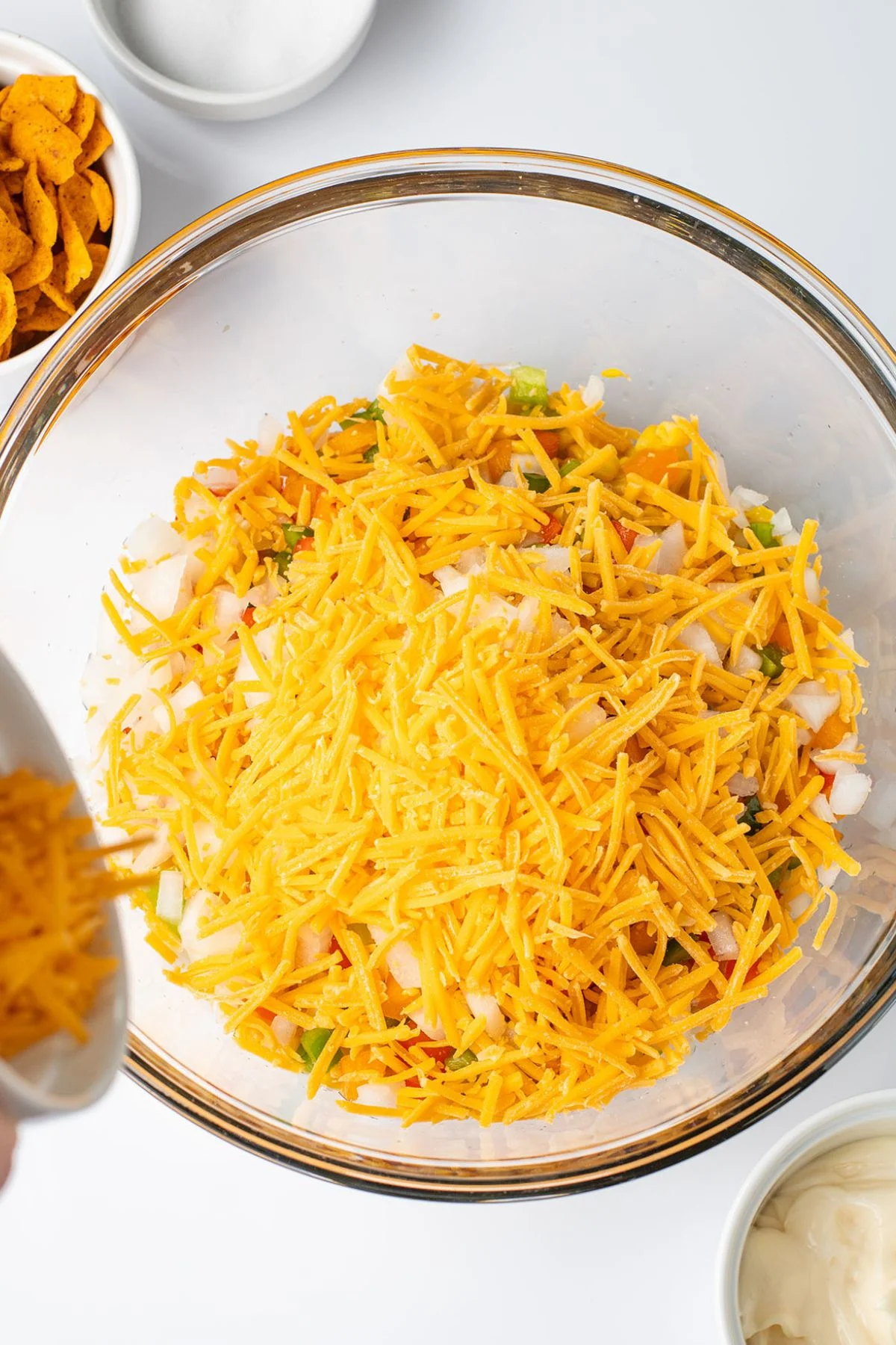 Corn, diced onion, bell peppers, and cheese in a glass mixing bowl.