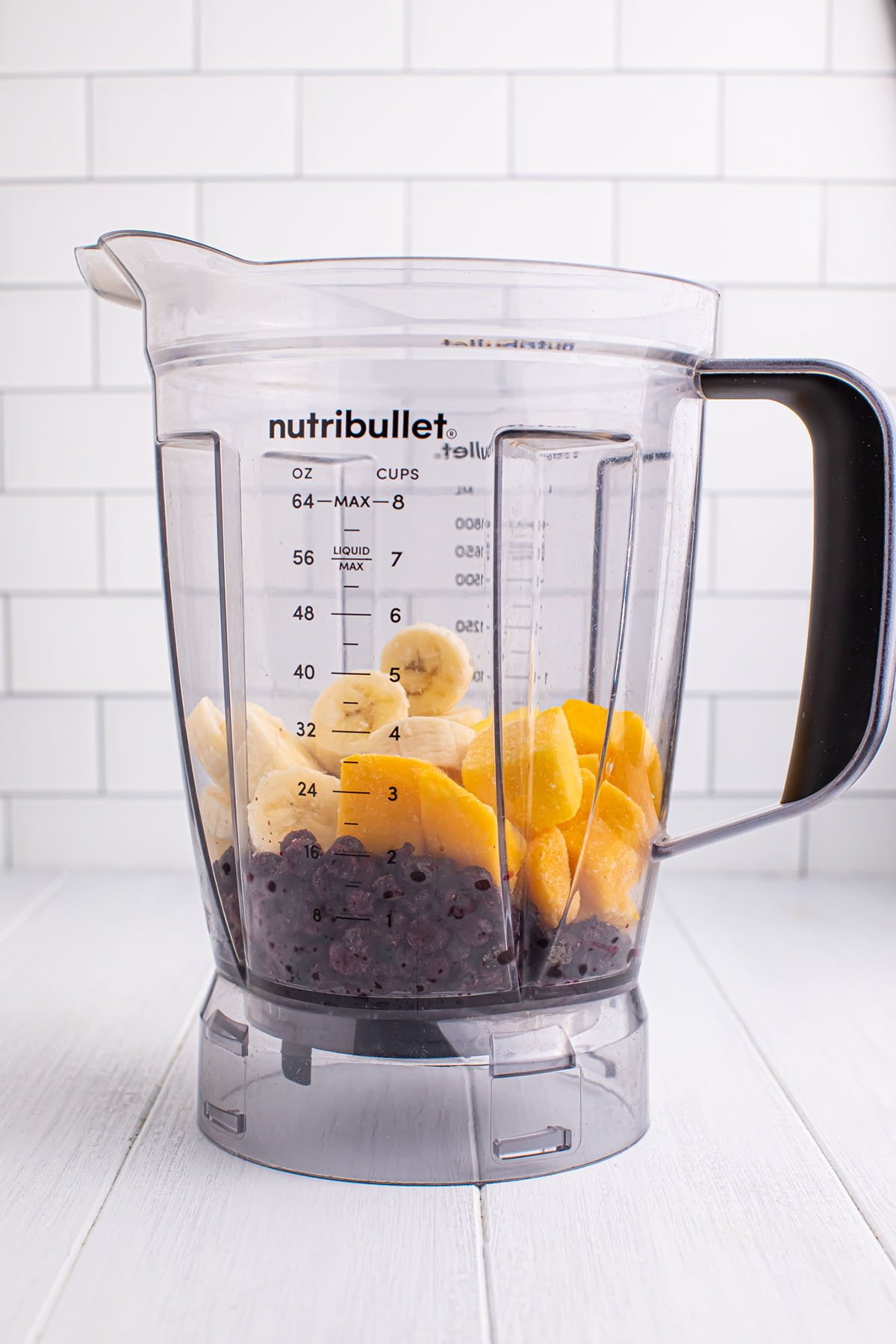 Frozen blueberries, frozen mango chunks, and a sliced banana in a blender.